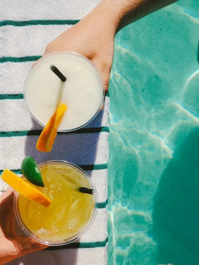 Tourists holding drinks above a pool